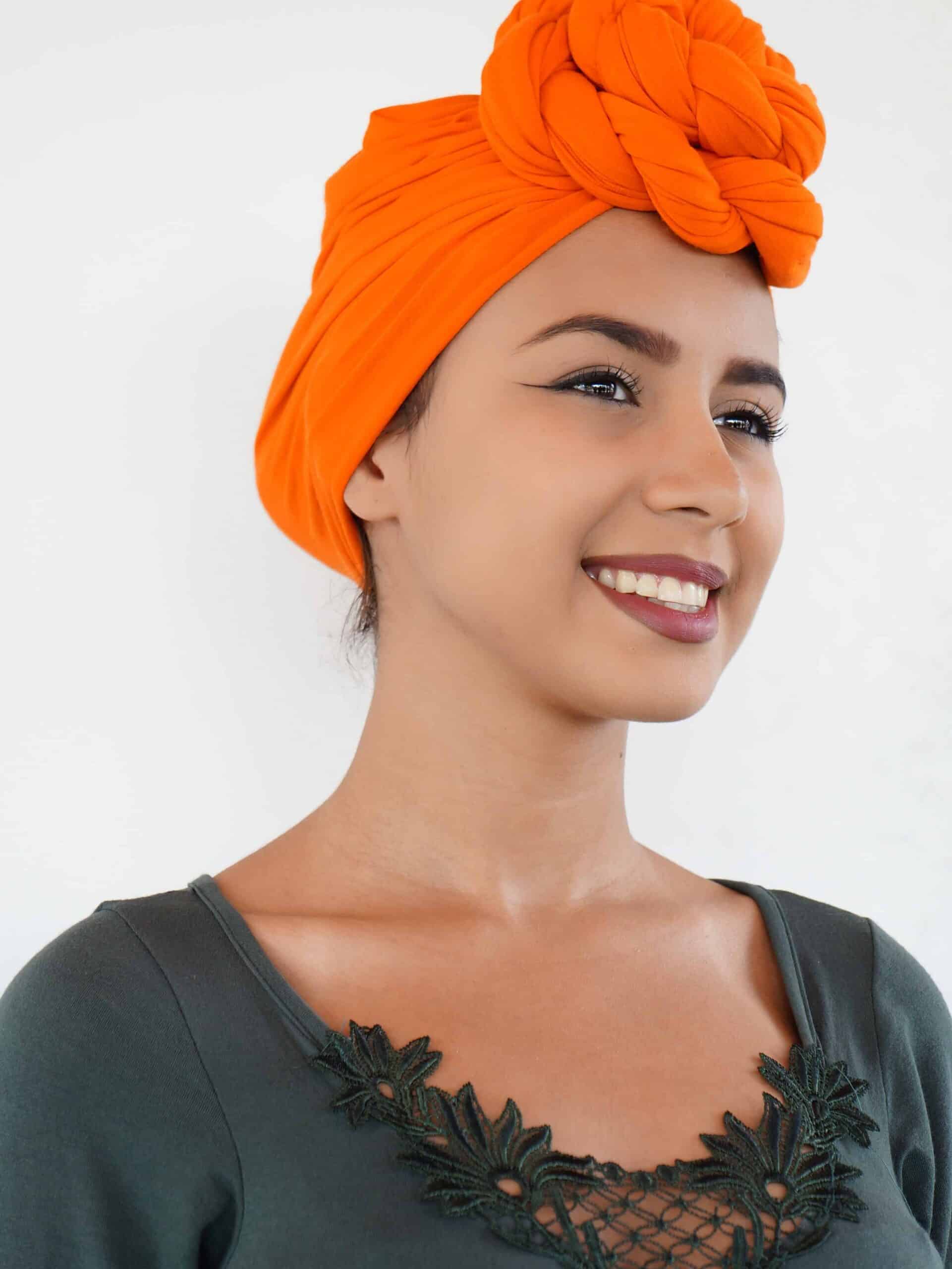 Oranje hoofddoek met sierlijke draaiknoop bovenop.